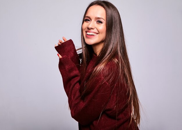 Portrait of beautiful happy cute brunette woman model in casual warm red sweater clothes isolated on gray with evening makeup and colorful lips