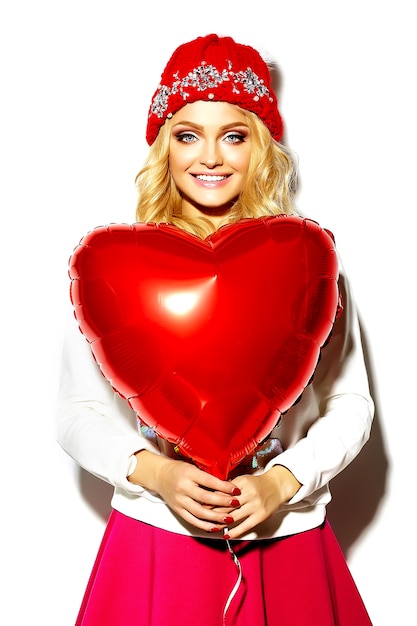 Free Photo portrait of beautiful happy sweet cute smiling blonde woman woman in casual hipster clothes, in pink skirt and winter warm beanie with red heart balloon in hands