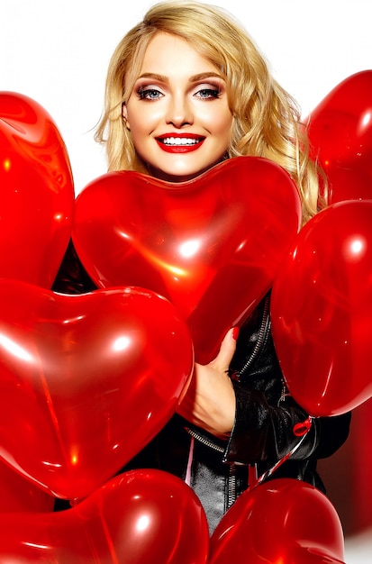 Free photo portrait of beautiful happy sweet smiling blonde woman girl holding in her hands red heart balloons in casual black hipster clothes