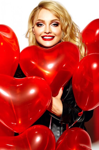 portrait of beautiful happy sweet smiling blonde woman girl holding in her hands red heart balloons in casual black hipster clothes