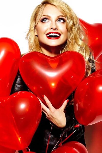 portrait of beautiful happy sweet smiling blonde woman girl holding in her hands red heart balloons in casual black hipster clothes