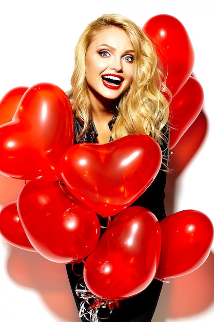 Free photo portrait of beautiful happy sweet smiling blonde woman girl holding in her hands red heart balloons in casual black hipster clothes