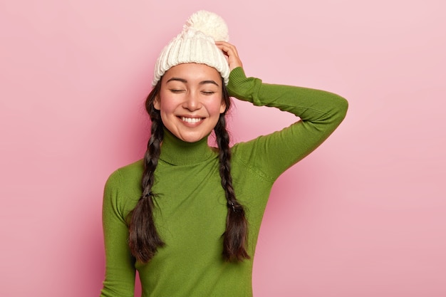 Free photo portrait of beautiful hipster girl, keeps eyes shut, dressed in green poloneck and hat, satisfied after spending free time with close person remembers pleasant moment during romantic date