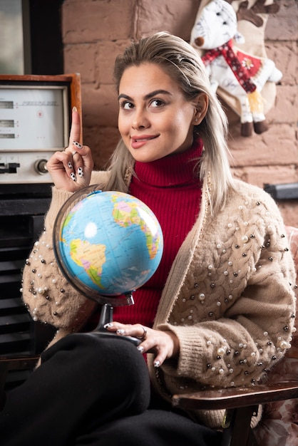 Free photo portrait of beautiful lady pointing up and holding a world globe