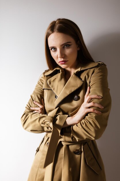 Portrait of beautiful lady in trench coat standing and mysteriously looking in camera