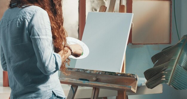 Portrait of a beautiful longhaired female artist at work at her canvas in a studio