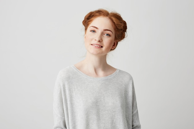 Portrait of beautiful redhead girl with buns and freckles smiling .