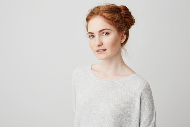 Portrait of beautiful redhead girl with buns and freckles smiling .