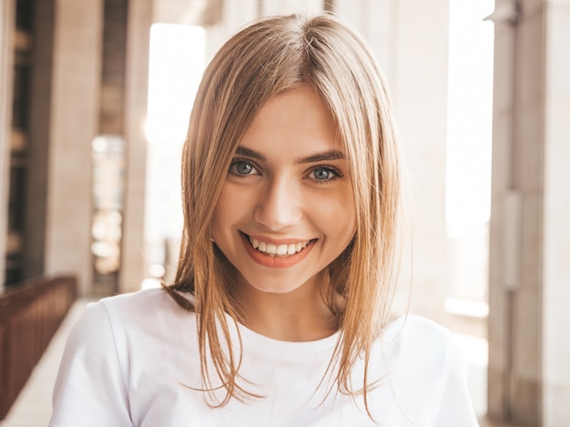 Portrait of beautiful smiling blond model dressed in summer hipster  clothes. Trendy girl posing in the street background. Funny and positive woman