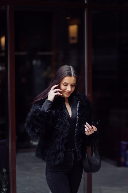 Portrait of a beautiful smiling girl with long dark hair wearing black .Young woman using  mobile phone