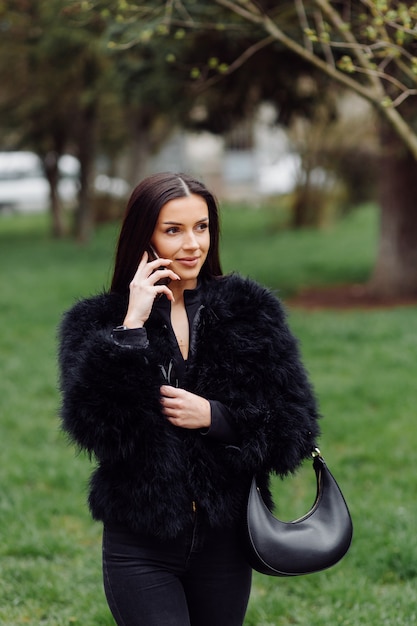 Free photo portrait of a beautiful smiling girl with long dark hair wearing black .young woman using  mobile phone