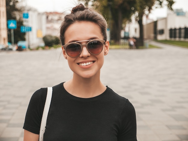 Portrait of beautiful smiling model dressed in summer clothes. Trendy girl posing in the street in sunglasses. Funny and positive woman having fun