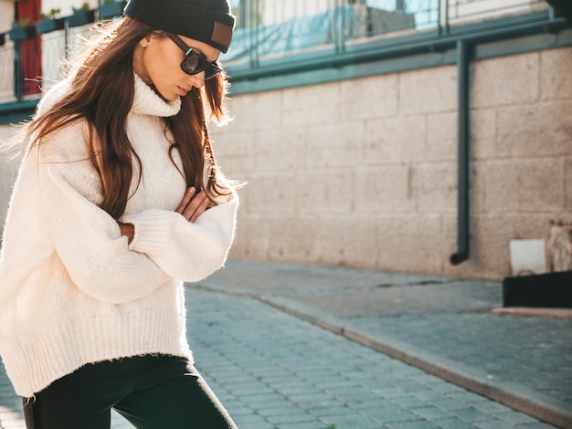 Free Photo portrait of beautiful smiling model. female dressed in warm hipster white sweater and beanie. trendy woman posing in the street