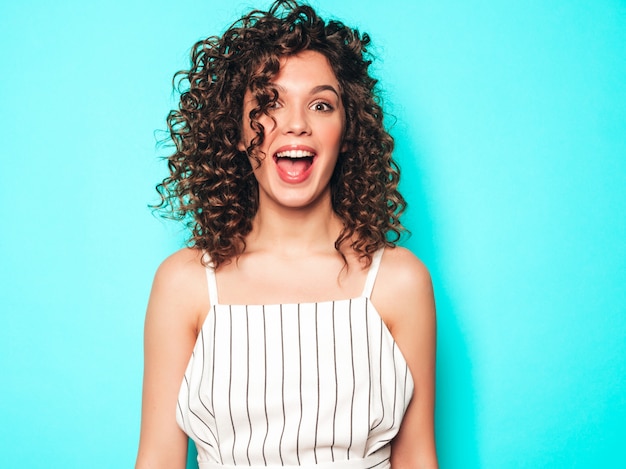 Portrait of beautiful smiling model with afro curls hairstyle dressed in summer hipster clothes.Sexy carefree girl posing near blue wall.Trendy funny and positive woman