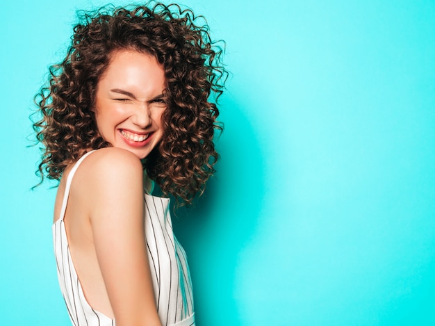 Portrait of beautiful smiling model with afro curls hairstyle dressed in summer hipster clothes.Sexy carefree girl posing near blue wall.Trendy funny and positive woman