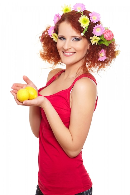 Free photo portrait of beautiful smiling redhead ginger woman in red cloth with yellow pink colorful flowers in hair isolated on white with lemon in hands