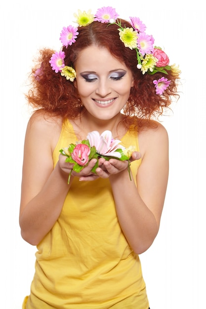 Portrait of beautiful smiling redhead ginger woman in yellow cloth with yellow pink colorful flowers in hair isolated on white holding flowers