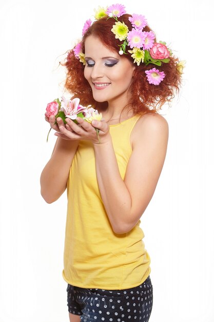 Portrait of beautiful smiling redhead ginger woman in yellow cloth with yellow pink colorful flowers in hair isolated on white holding flowers