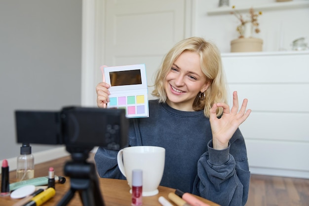 Portrait of beautiful smiling woman recording video in her room has camera on coffee table reviewing