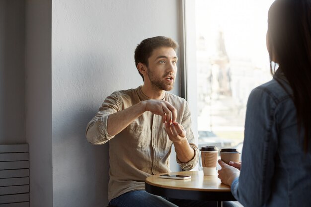 Portrait of beautiful unshaved freelance designer, sitting in cafe on meeting with customer trying to explain conception of his work and expressive gesticulating with hands.