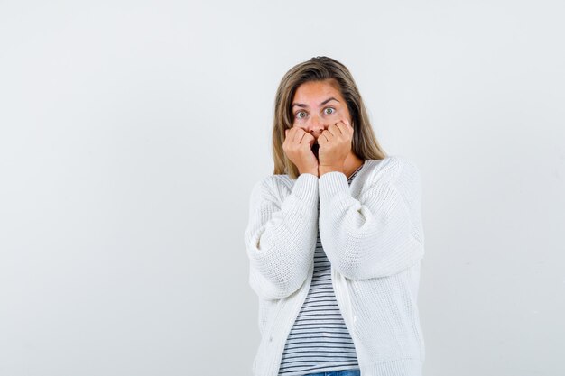 Portrait of beautiful woman biting fists emotionally in jacket, t-shirt and looking scared front view