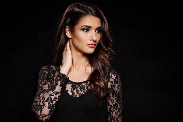 Portrait of beautiful woman in black dress over dark wall