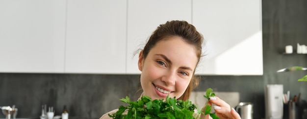 Free photo portrait of beautiful woman cooking holding fresh parsley adding herbs while making salad healthy