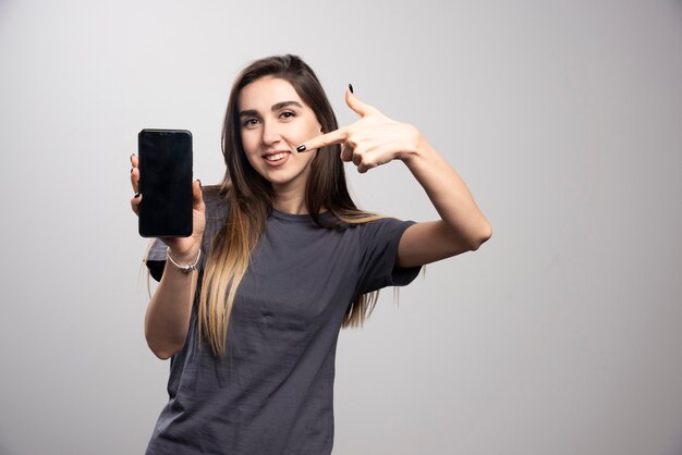 Portrait of beautiful woman holding a modern cell isolated over gray wall.