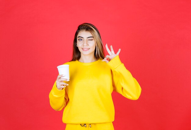 Portrait of beautiful woman holding plastic cup of tea and giving ok sign