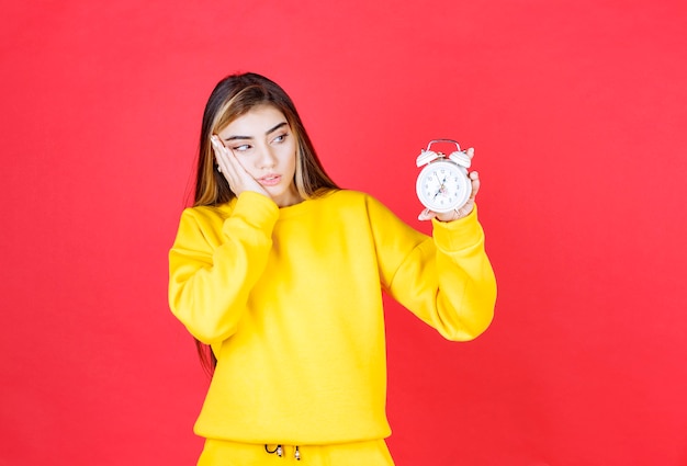 Portrait of beautiful woman looking at time on clock on red wall