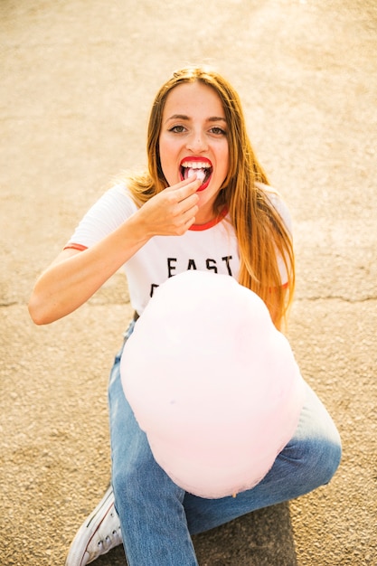 Free photo portrait of a beautiful woman sitting on street eating candy floss