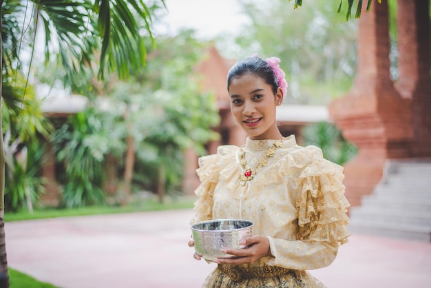 Free photo portrait beautiful woman in songkran festival with thai traditional costume in the temple holding water bowl and smile thailand culture with water festival