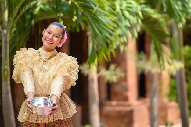 Free photo portrait beautiful woman in songkran festival with thai traditional costume in the temple holding water bowl and smile thailand culture with water festival