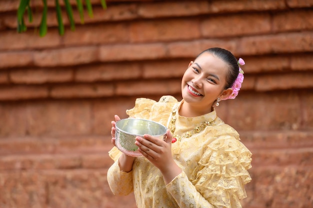 Portrait beautiful woman in Songkran festival with Thai Traditional costume in the temple holding water bowl and smile Thailand culture with Water festival