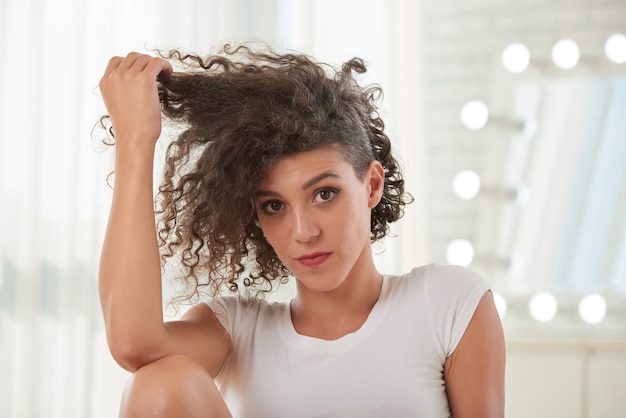 Portrait of beautiful woman touching her curly hair looking at camera