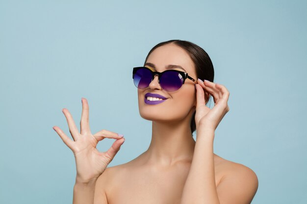 Portrait of beautiful woman with bright make-up and sunglasses on blue studio