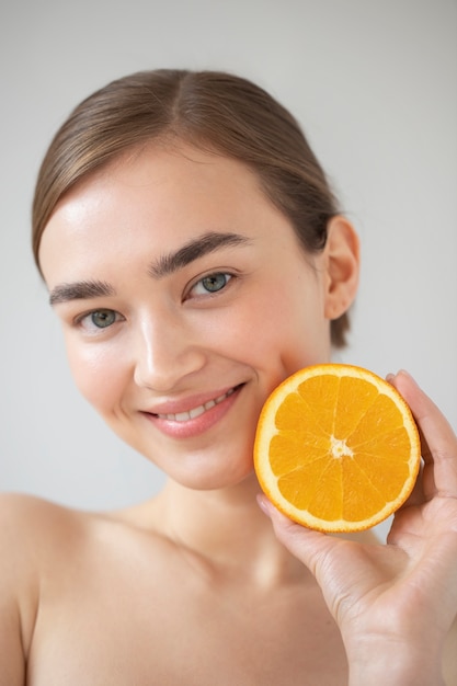 Free photo portrait of beautiful woman with clear skin holding sliced orange fruit