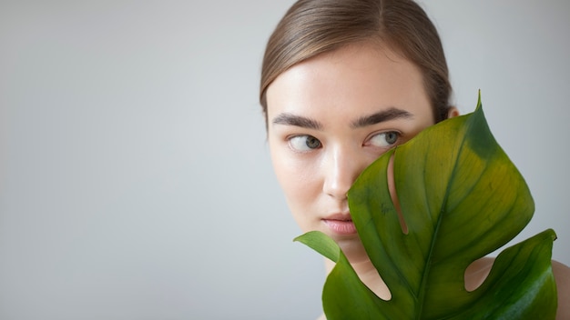 Free photo portrait of beautiful woman with clear skin posing with monster plant leaf