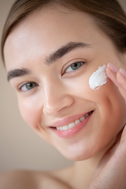 Portrait of beautiful woman with clear skin using moisturizer on her face