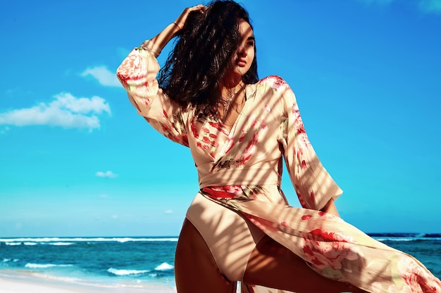 Portrait of beautiful woman with dark long hair in beige dress posing on summer beach