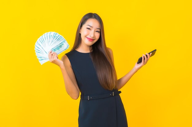 Portrait beautiful young asian business woman with a lot of cash and money on yellow background