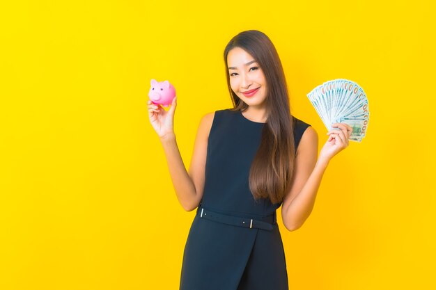 Portrait beautiful young asian business woman with a lot of cash and money on yellow background