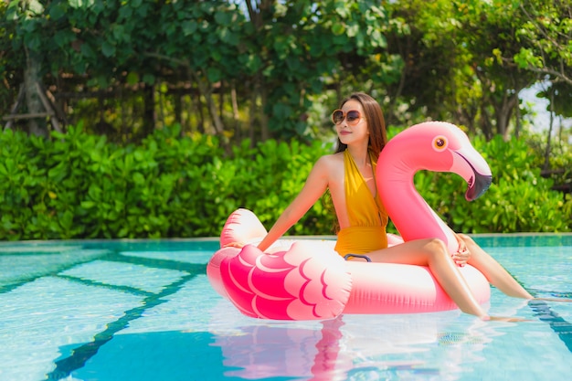 Portrait beautiful young asian woman on the flamingo inflatable float in swimming pool at hotel resort