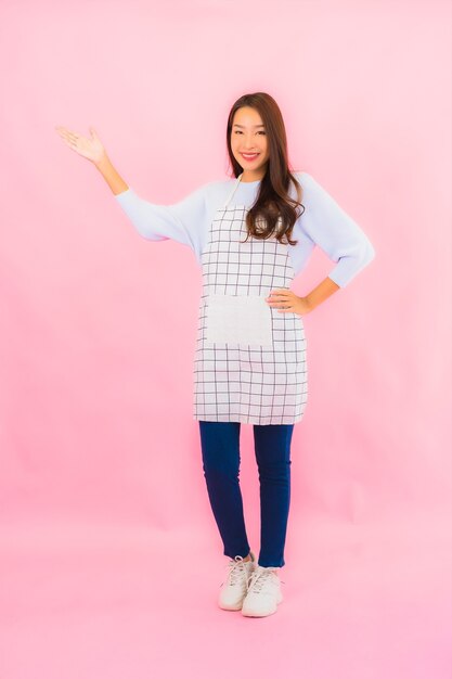 Portrait beautiful young asian woman in kitchen wear with apron on pink isolated wall