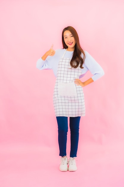 Portrait beautiful young asian woman in kitchen wear with apron on pink isolated wall