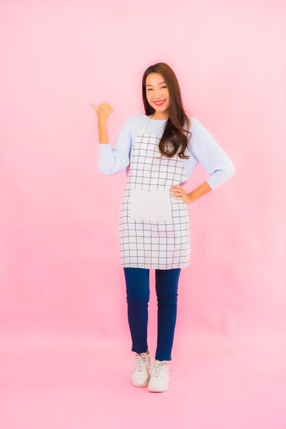 Portrait beautiful young asian woman in kitchen wear with apron on pink isolated wall