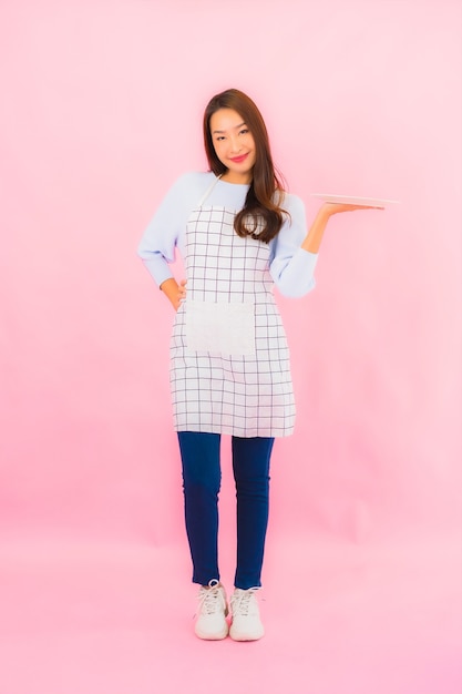 Portrait beautiful young asian woman in kitchen wear with apron on pink isolated wall