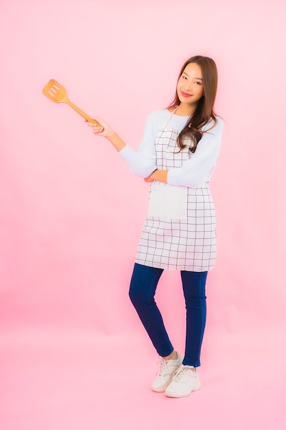 Portrait beautiful young asian woman in kitchen wear with apron on pink isolated wall