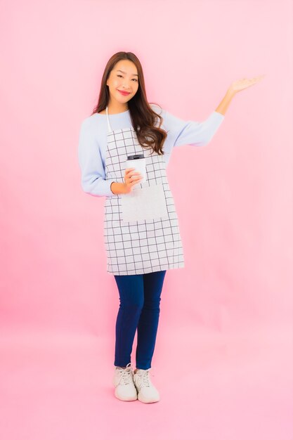 Portrait beautiful young asian woman in kitchen wear with apron on pink isolated wall