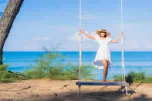 Free photo portrait beautiful young asian woman relax smile on swing around beach sea ocean for nature travel in vacation